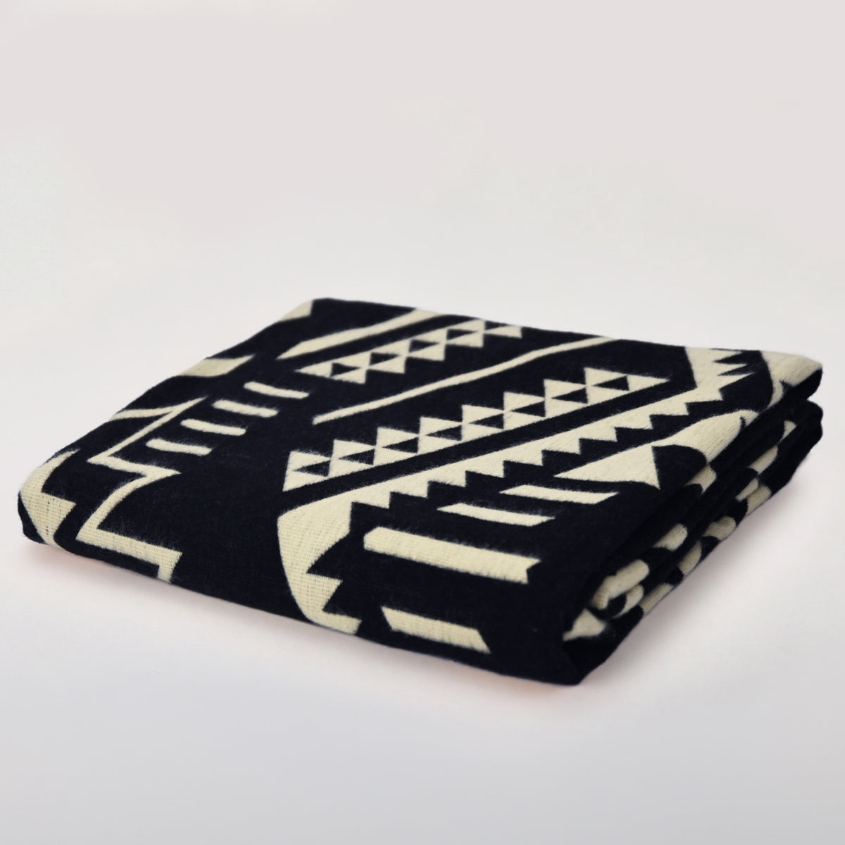 Opgevouwen omkeerbare Aztec Black and Beige alpacadeken op een lichte achtergrond