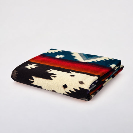 A folded alpaca blanket with a Southwestern geometric pattern in black, cream, red, orange, and blue