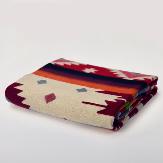 Folded Aztec Red Geometric alpaca blanket in red, ivory and earthy tones on a light background