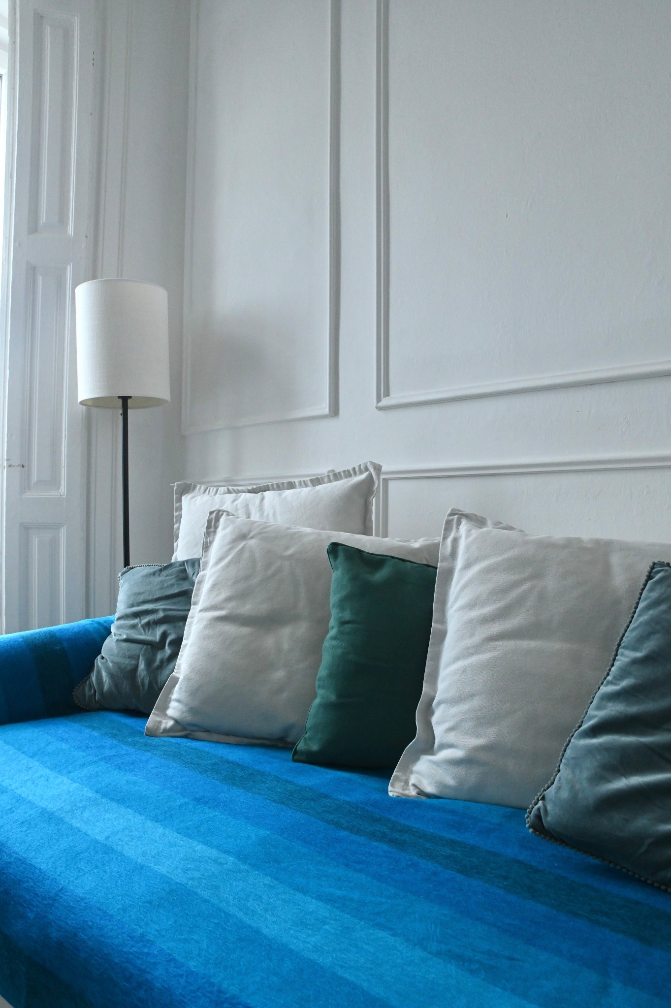 Blue alpaca blanket on the sofa with decorative pillows against a white paneled wall.