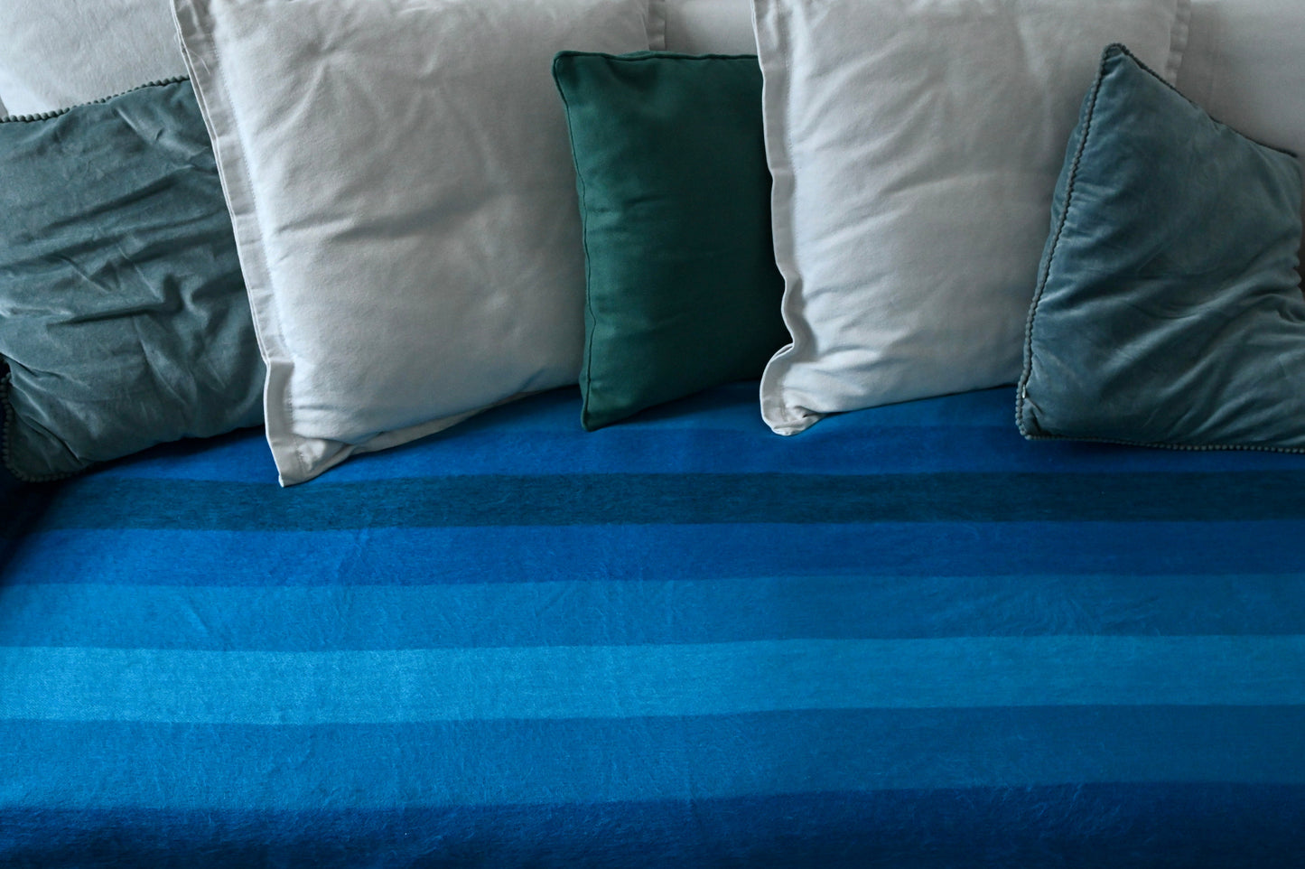 Blue striped blanket with green and gray pillows on a bed