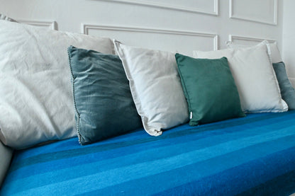 Blue striped alpaca blanket with green and white pillows on a sofa against a white paneled wall.