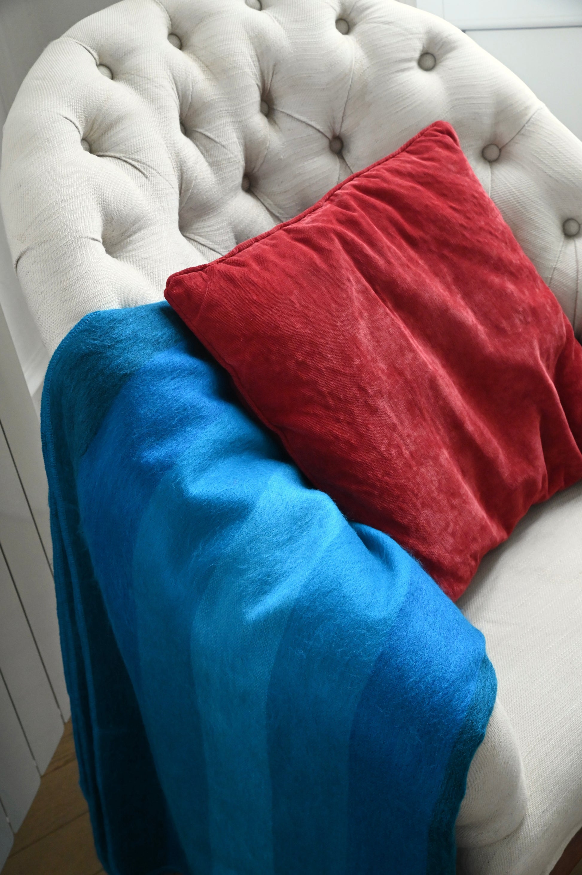 Blue alpaca blanket and red pillow on a white tufted chair