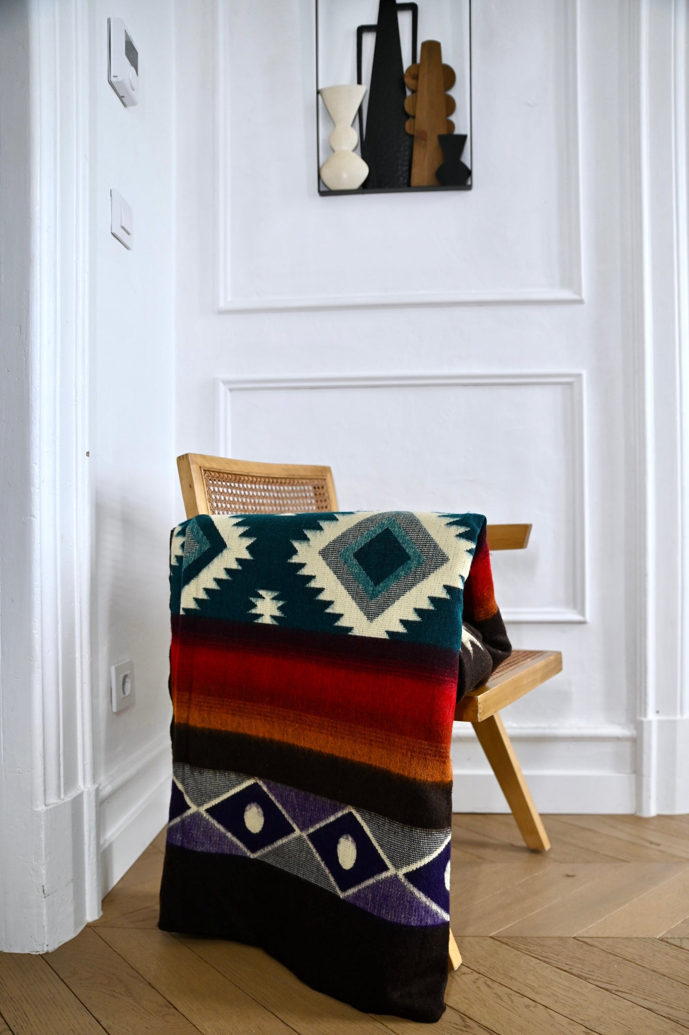 Colorful patterned alpaca blanket draped over a wooden chair against a white wall.