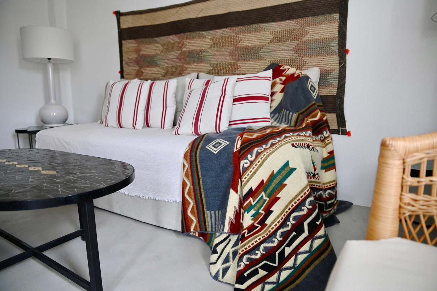Living room with a sofa covered by patterned alpaca blanket and pillows, next to a side table with a lamp.