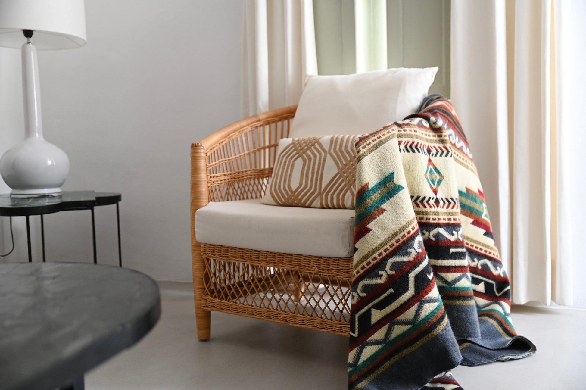 Wicker chair with patterned alpaca throw and pillows in a room with a lamp and table.