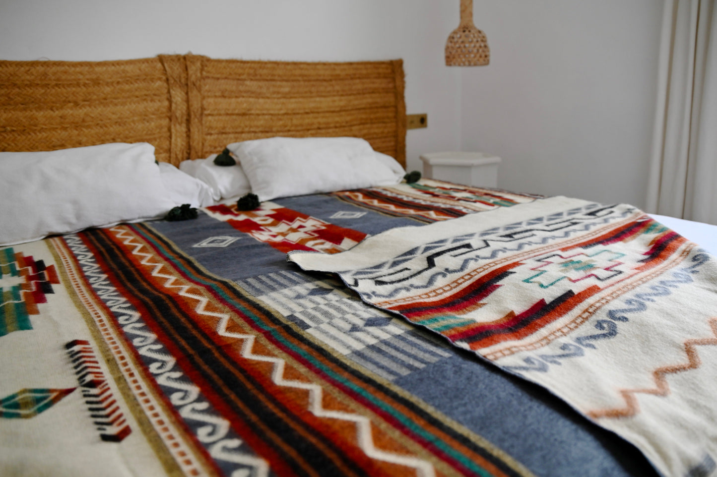 Bed with a patterned alpaca blanket and wooden headboard in a bedroom setting.