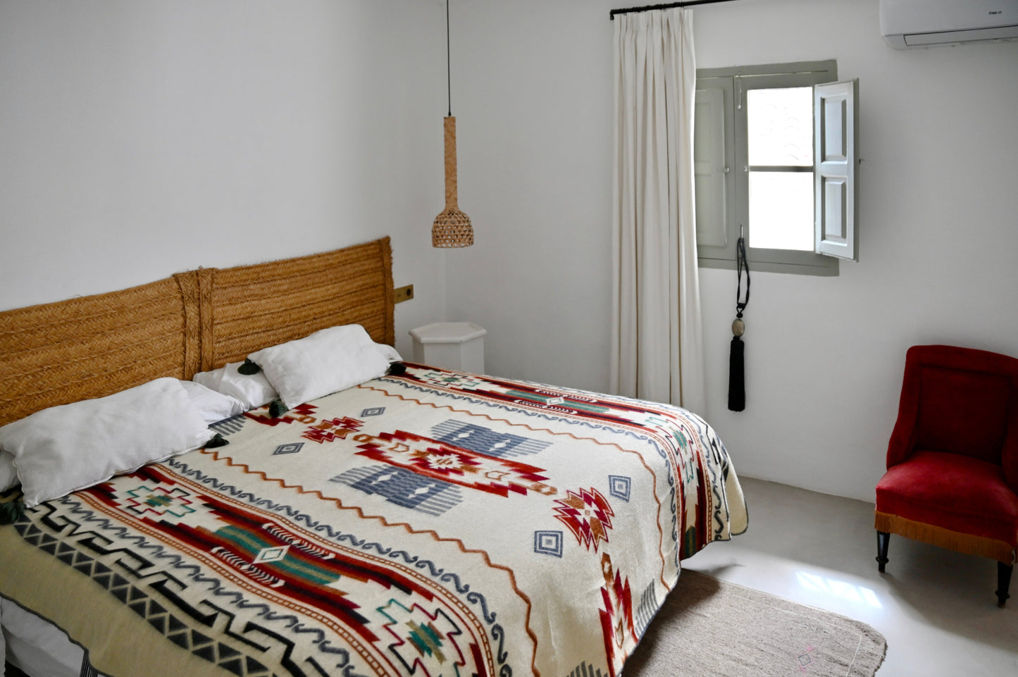 Bedroom with a bed featuring a patterned alpaca blanket, wooden headboard, and a red chair.