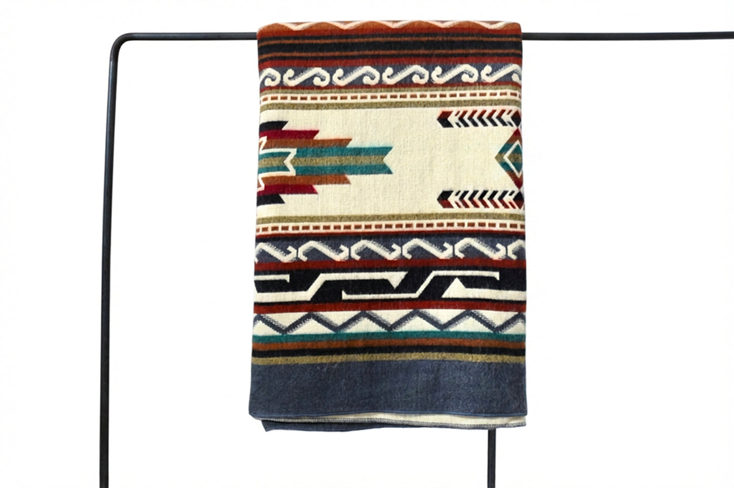 Patterned alpaca blanket draped over a black metal rod on a white background