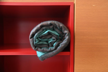 Rolled Emerald Forest alpaca wool blanket on a red shelf