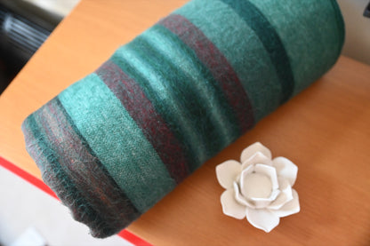 Folded Emerald Forest alpaca blanket beside a white ceramic flower