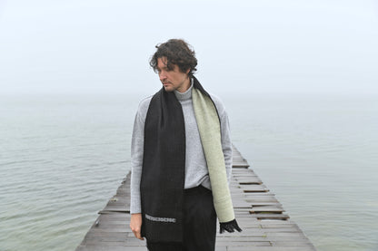 Person wearing a black and beige scarf on a wooden dock by a body of water