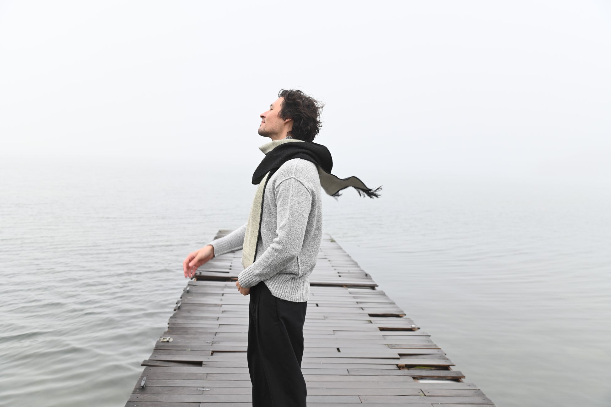 Man wearing a charcoal and ivory alpaca wool scarf outdoors by the water